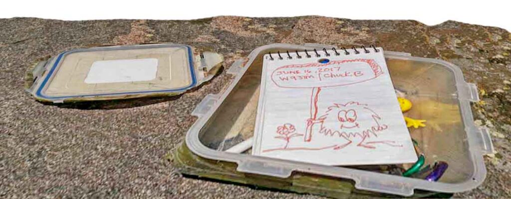 Un tesoro de geocaching tipo tupperware escondido en la naturaleza, mostrando su interior con el libro de registro y un bolígrafo.